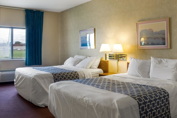 A hotel room with two beds, a large window with curtains, a wall-mounted lamp, and a framed picture.