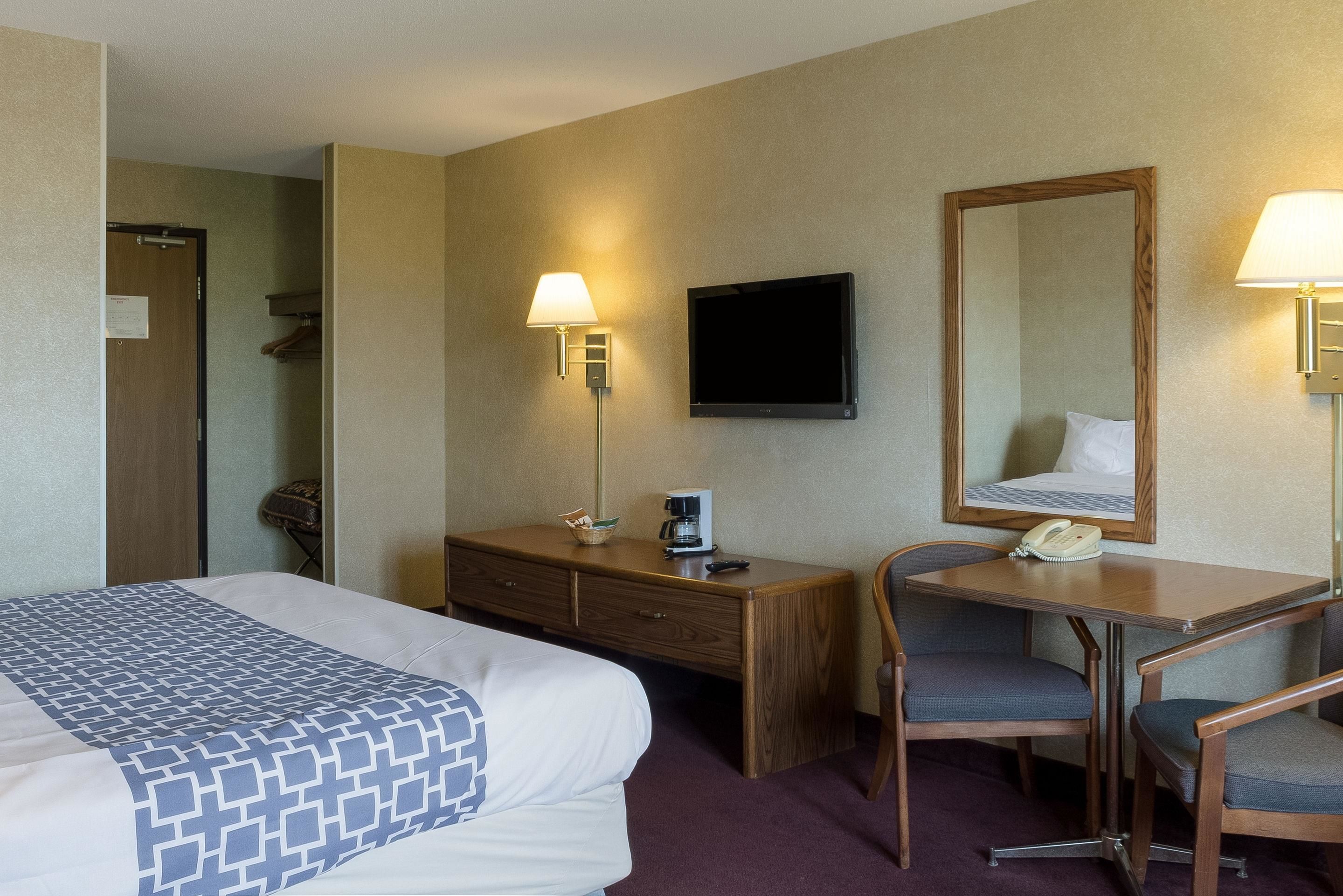 A hotel room with a bed, a desk, two chairs, a TV, a mirror, and two lamps.