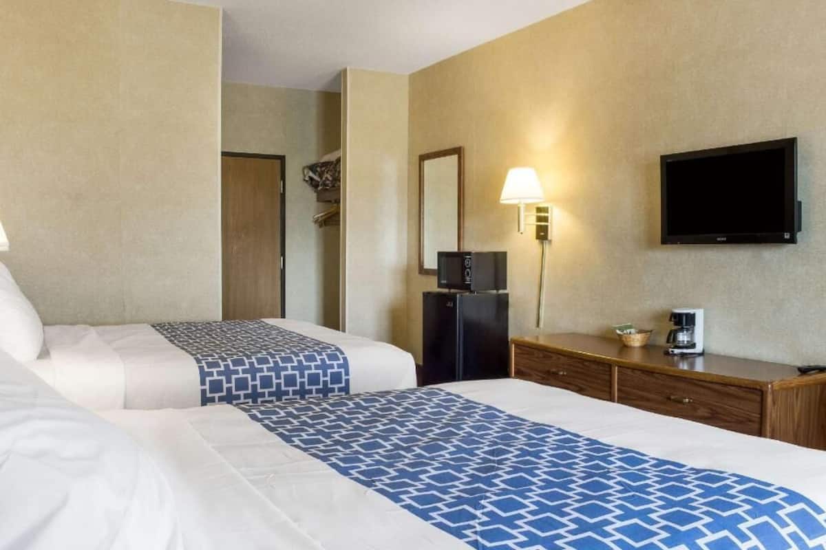 A hotel room with two beds, a TV, a refrigerator, a lamp, and a coffee maker.