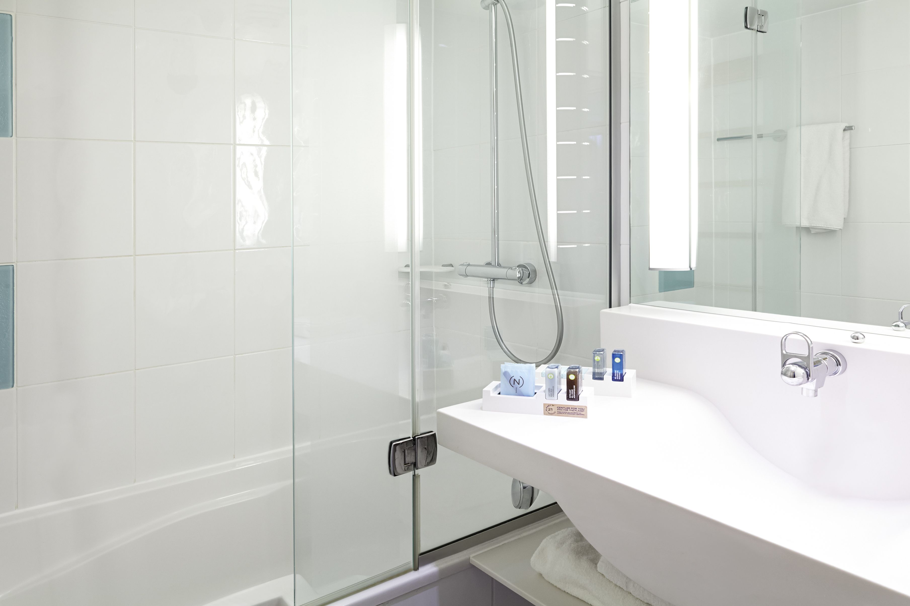 Une salle de bain moderne avec une douche à parois de verre, un lavabo blanc avec un miroir et des articles de toilette posés sur le comptoir.