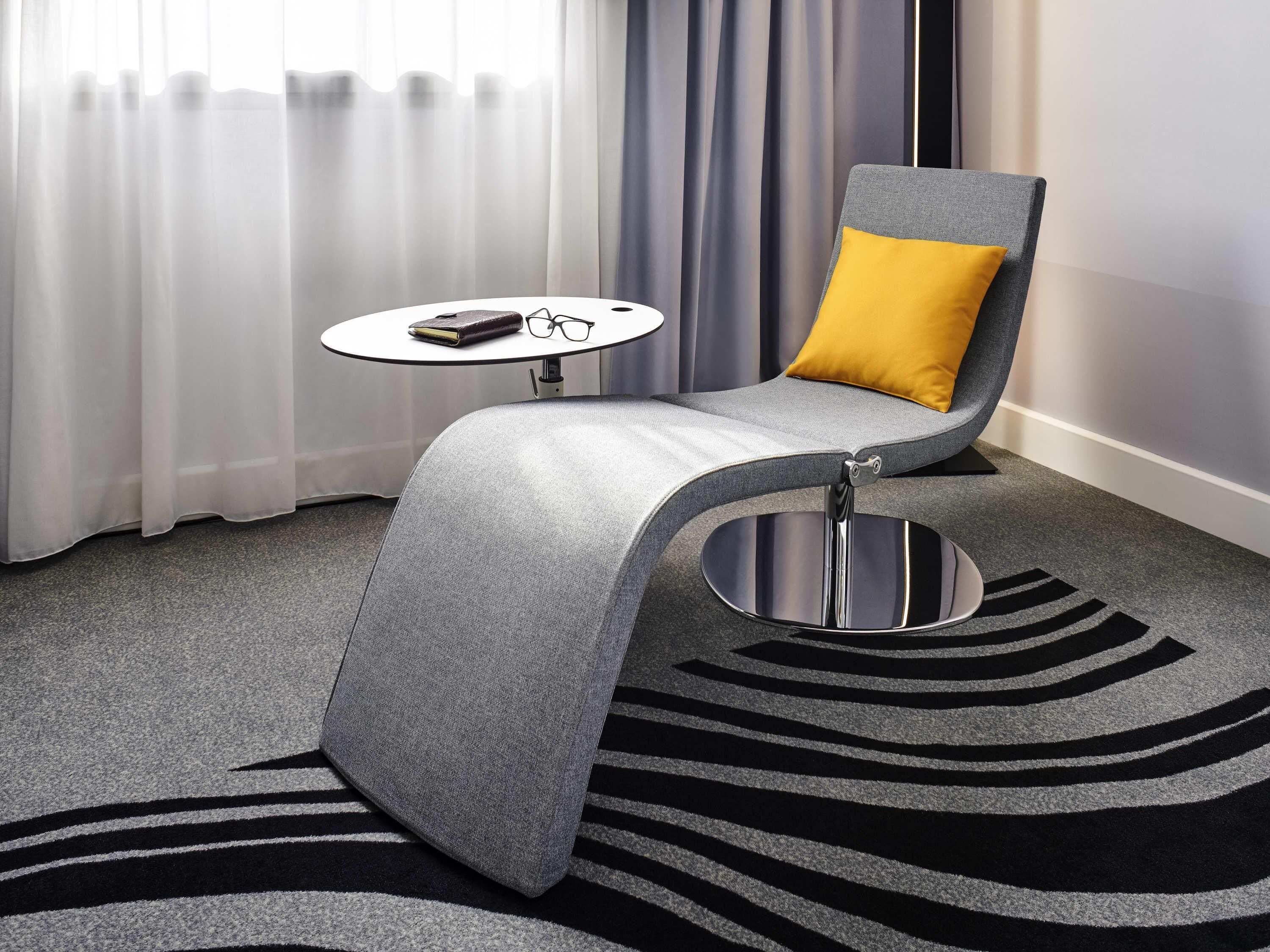 A modern room with a grey armchair, a small round table, and a zebra-striped rug.