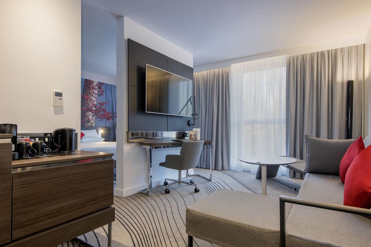 Una habitación de hotel moderna con televisión de pantalla plana, un escritorio con silla, un sofá y una estación de café.