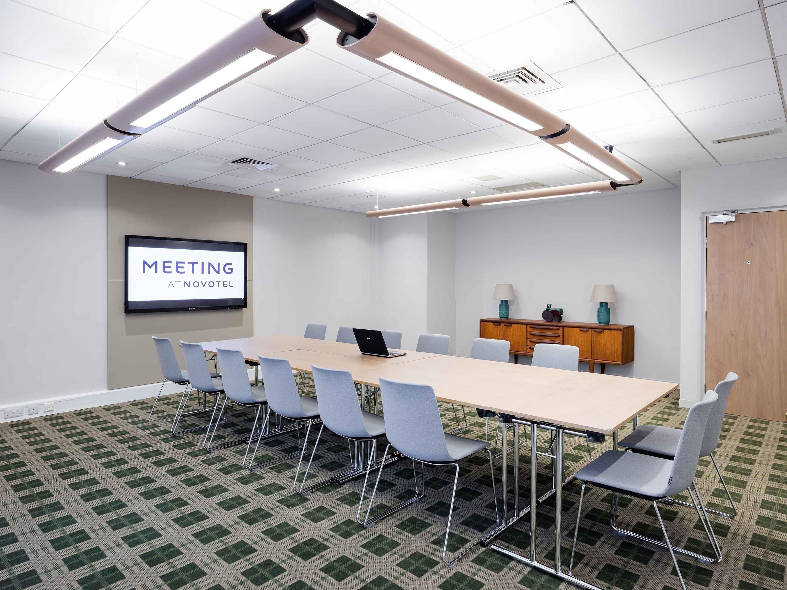 A conference room with a long table, six chairs, a projector screen, and a wooden cabinet with lamps.