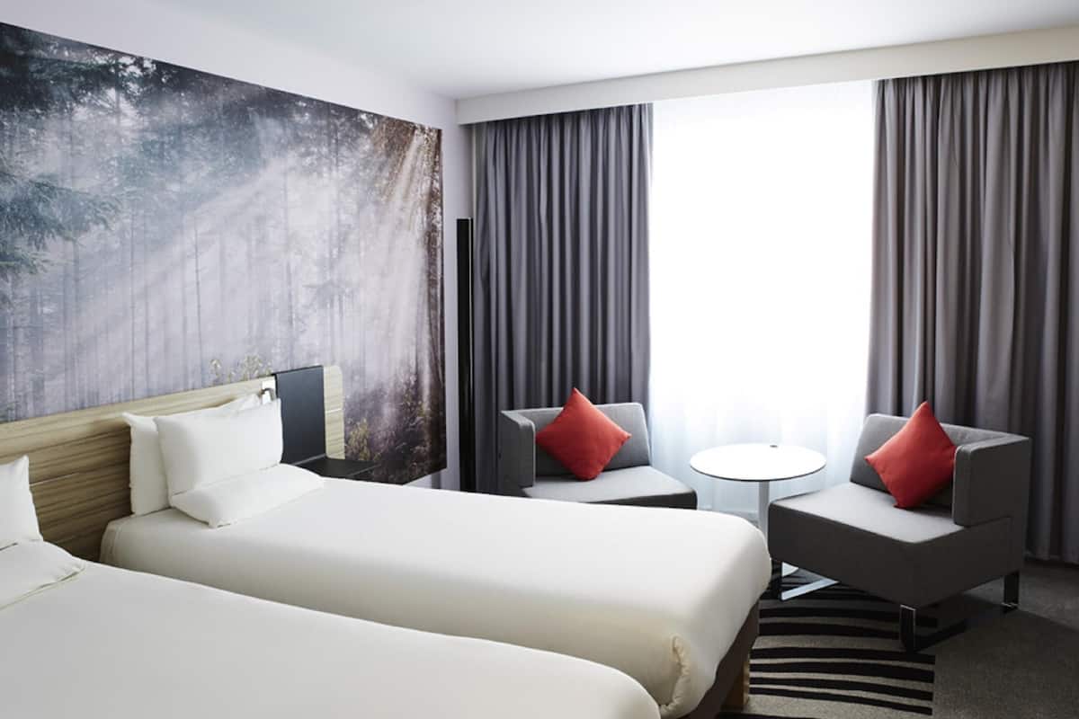 Habitación de hotel con dos camas, un escritorio, una silla, una mesita y vistas al exterior.