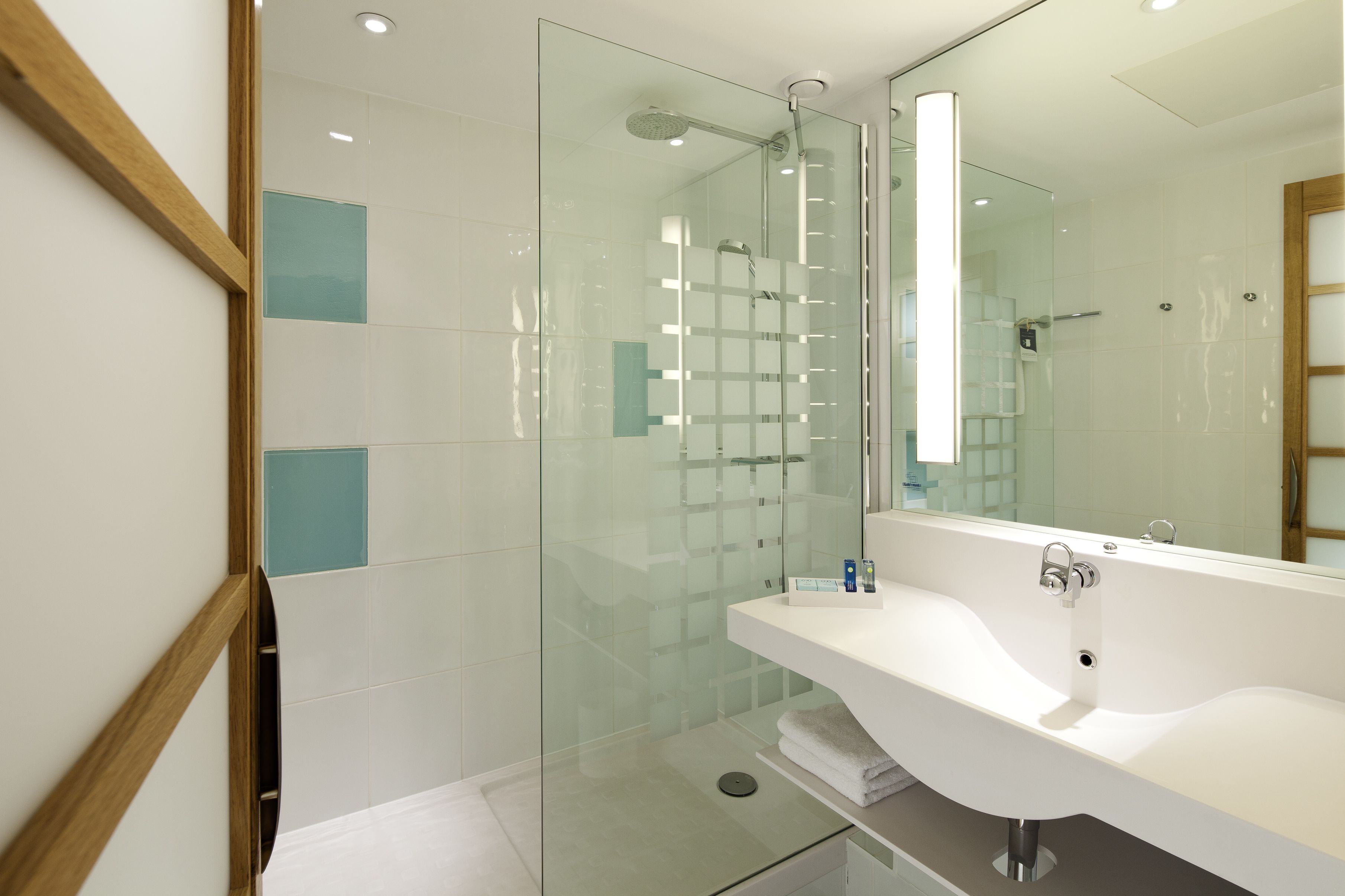 Un baño moderno con ducha de vidrio, lavamanos blanco y un espejo grande.