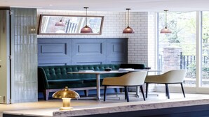 Ein modernes Interieur mit einem grünen Sofa, zwei Sessel, einem Tisch, Pendelleuchten und einem großen Fenster.