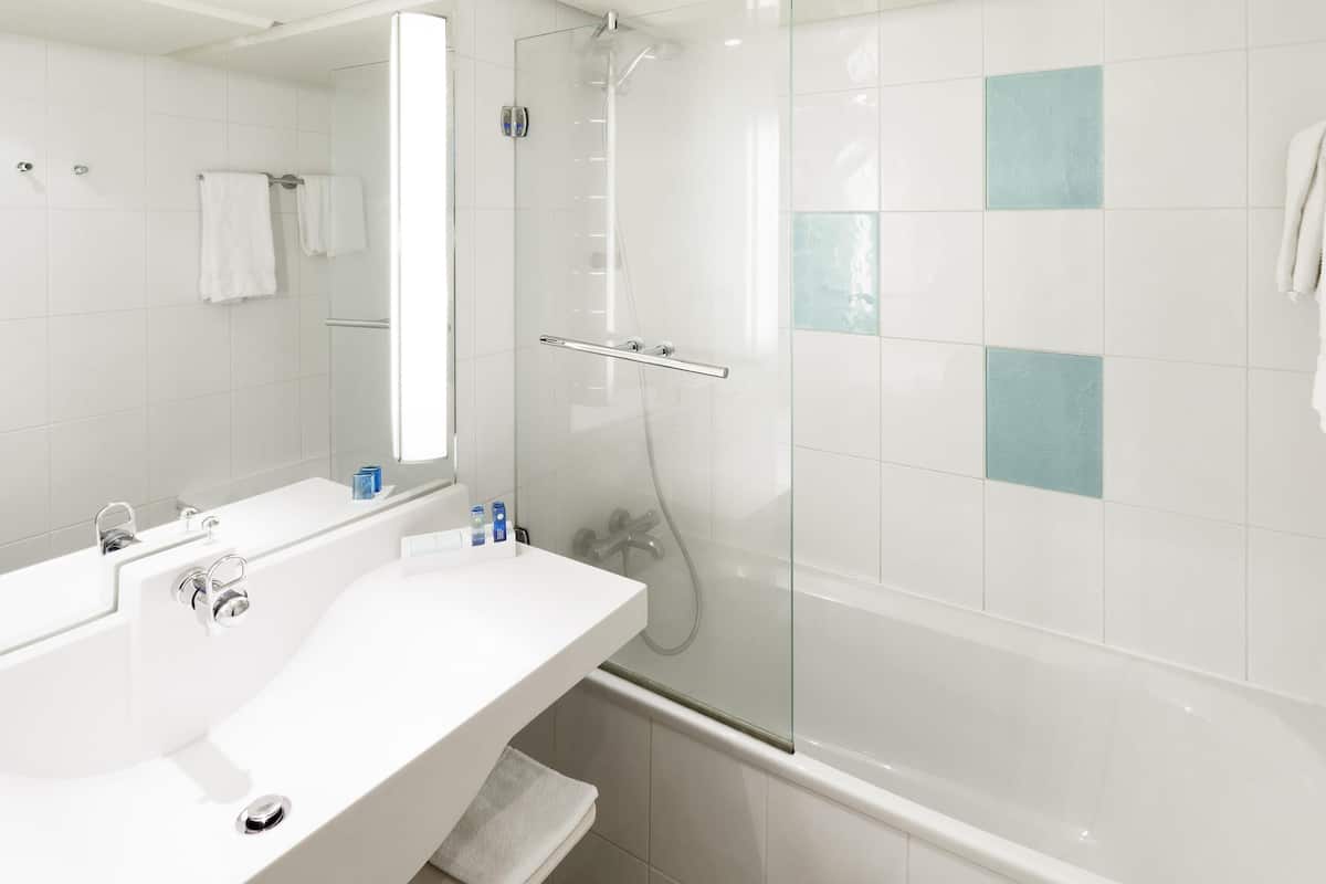 Une salle de bain moderne avec une douche à parois de verre, un lavabo blanc avec un miroir et une baignoire.