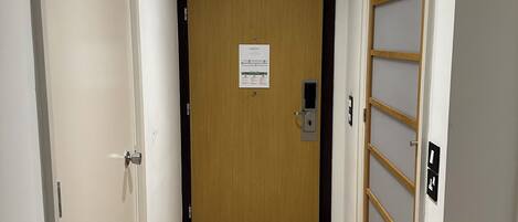 A hallway with a wooden door at the end, a light switch, and a fire alarm panel.