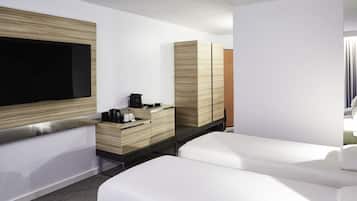 Quarto de hotel moderno com uma televisão de tela plana grande, um armário de madeira com cafeteira e duas camas brancas.
