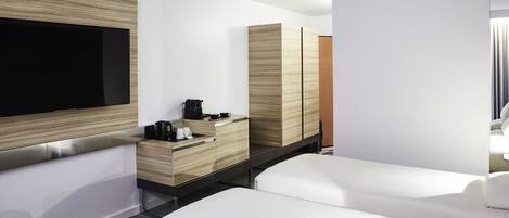 A modern hotel room with a large flat-screen TV, a wooden cabinet with a coffee maker, and two white beds.
