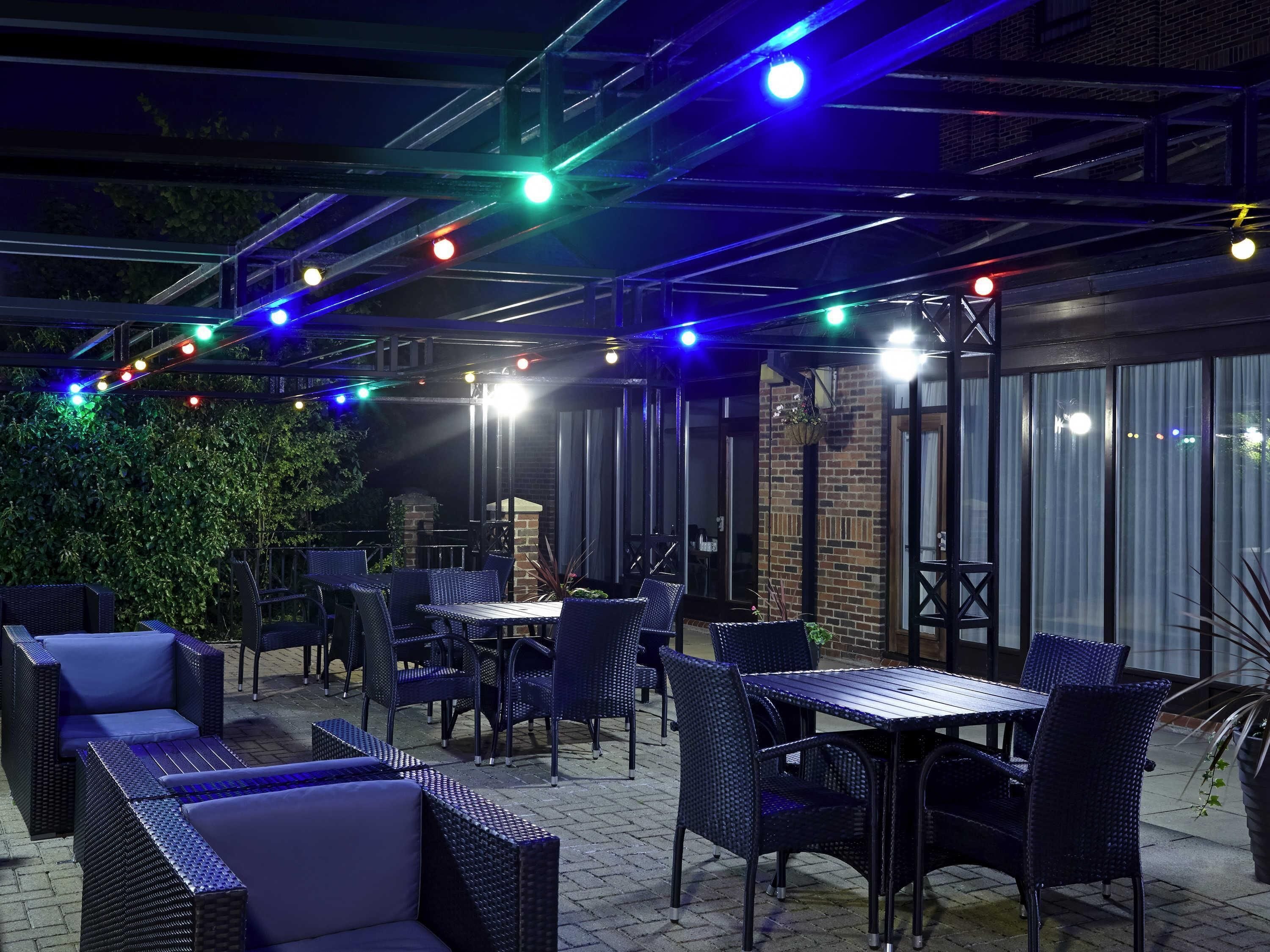 An outdoor patio area with tables and chairs, a brick wall, and string lights.