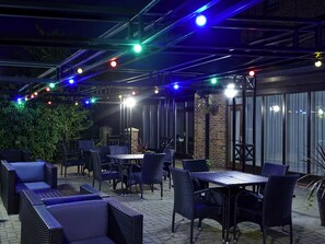 An outdoor patio area with tables and chairs, a brick wall, and string lights.