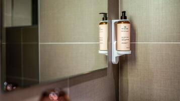Une salle de bain avec un miroir, une serviette et deux flacons de gel nettoyant pour les mains de la marque Nuxe, posés sur une étagère.