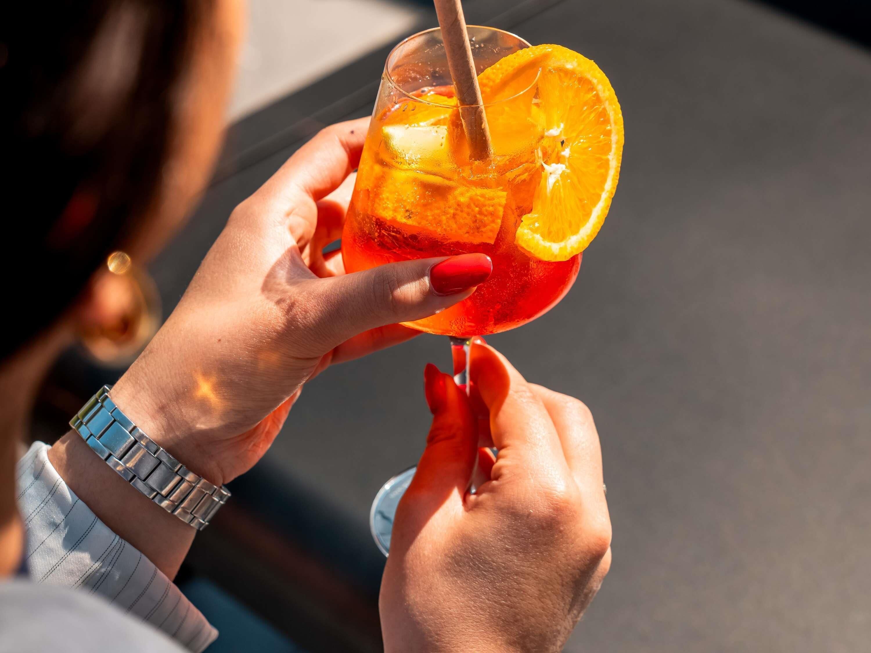 A person holding a glass with a red beverage and an orange slice.