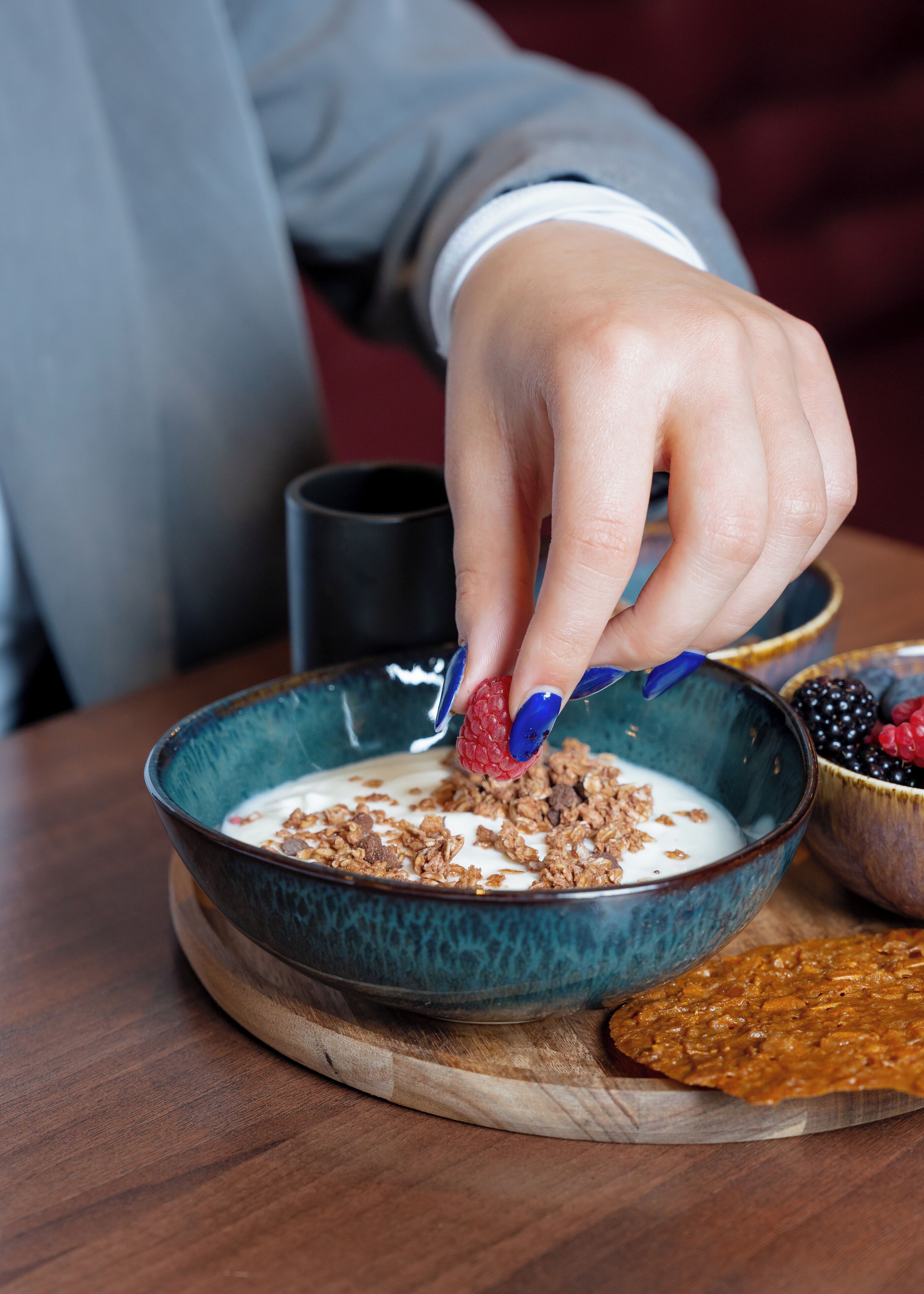 Uma tigela de cereal com iogurte e granola, uma fatia de torrada e uma tigela de frutas vermelhas sobre uma mesa de madeira.