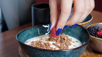 Uma tigela de cereal com iogurte e granola, uma fatia de torrada e uma tigela de frutas vermelhas sobre uma mesa de madeira.