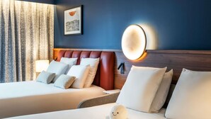 A hotel room with two beds, a plush octopus toy on the bed, a framed artwork on the wall, and a wall-mounted light fixture.