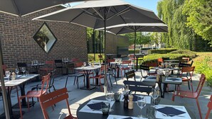 An outdoor dining area with brick walls, multiple tables and chairs, umbrellas, and a brick building in the background.