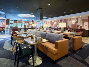 A modern restaurant with a central seating area featuring a sofa and tables, surrounded by chairs.