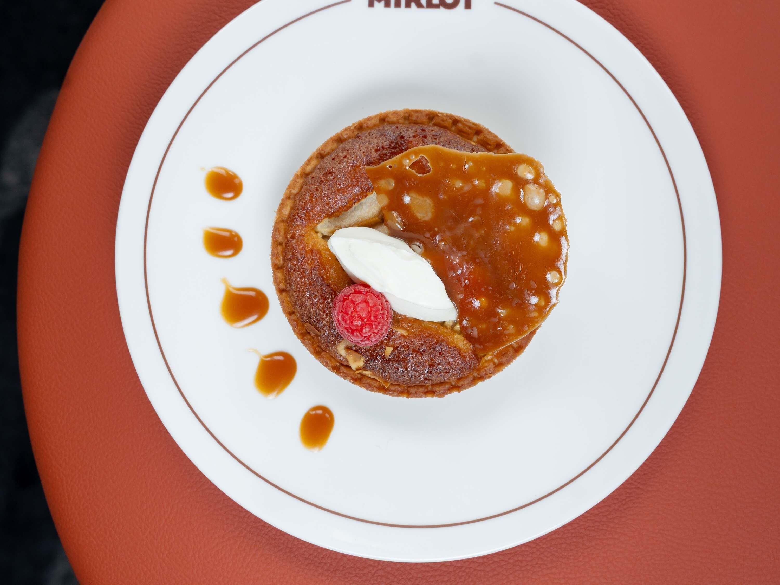 Un postre sobre un plato blanco, con salsa de caramelo y frambuesa.