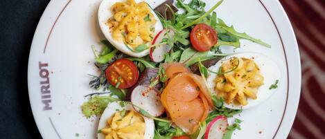 A plate of food with eggs, tomatoes, and greens on a white plate with a red rim.