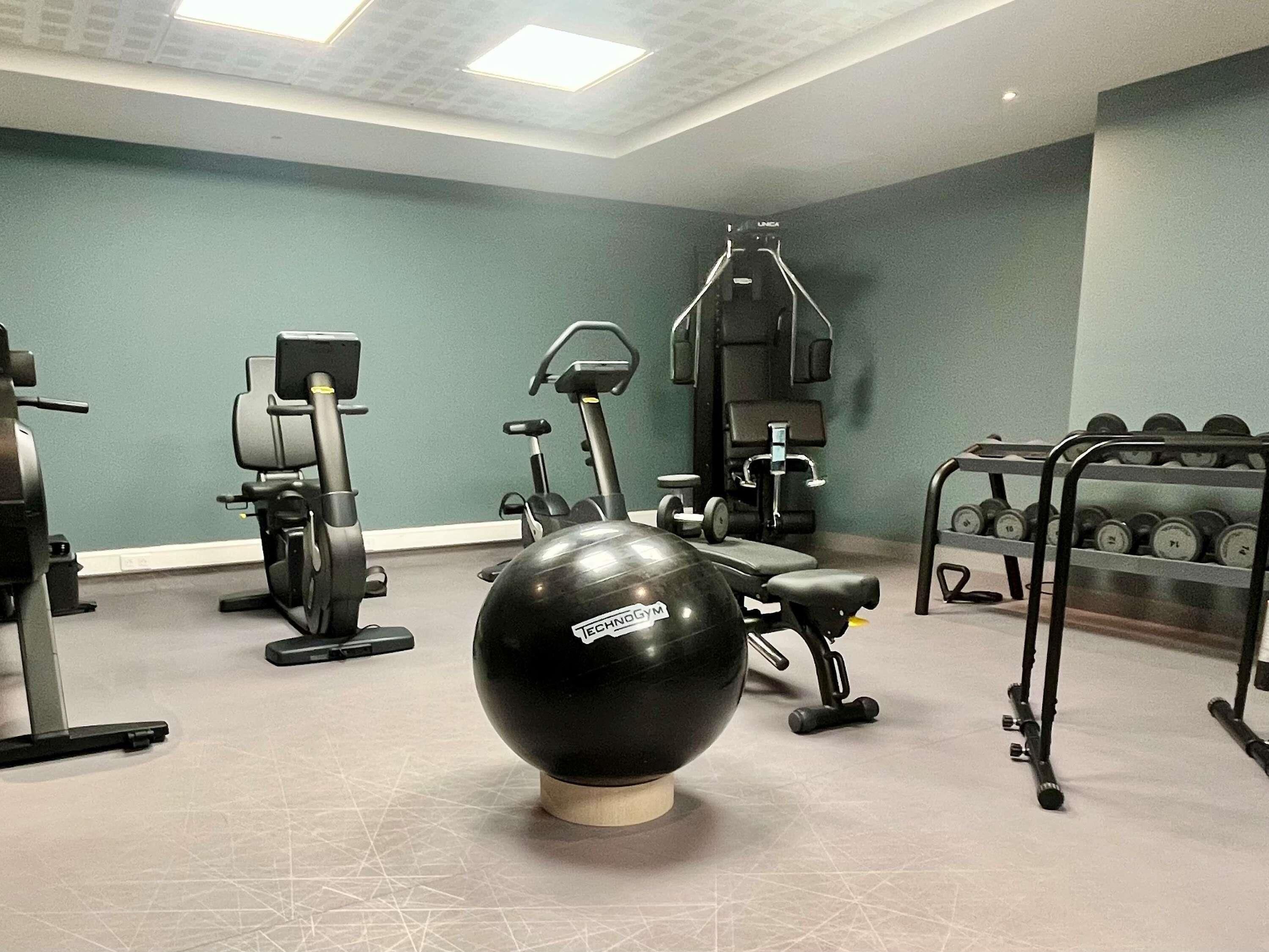 Un gimnasio con equipo de ejercicio, una pelota y mancuernas.
