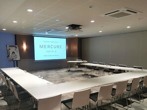 A conference room with a large screen displaying 'MERCURE HOTELS Coon Cote do Naara.'