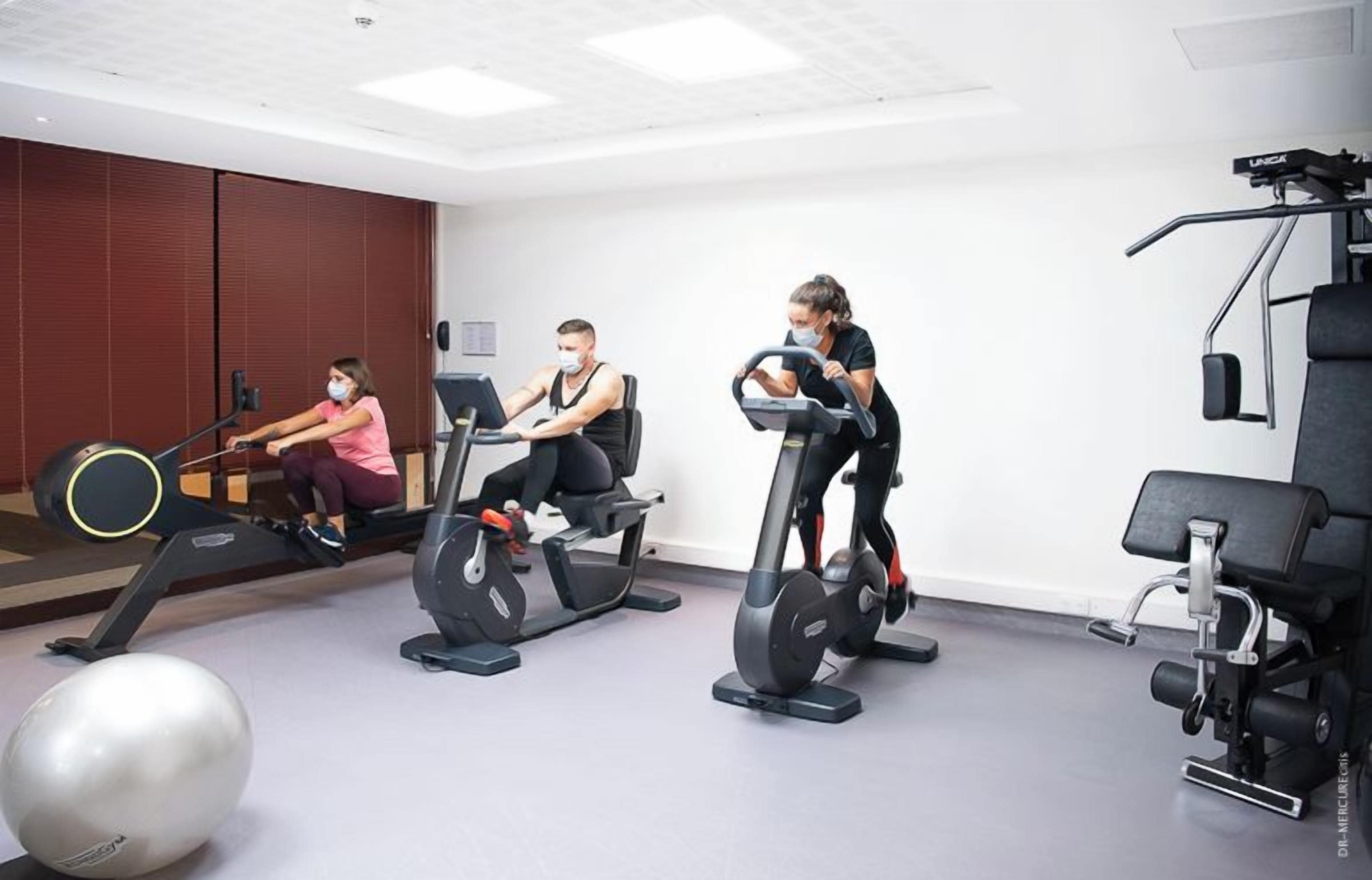 A gym with stationary bikes, a rowing machine, and weightlifting equipment.