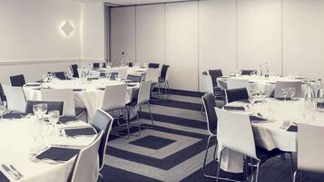 Un salón de conferencias con varias mesas redondas, cada una cubierta con manteles blancos, sillas y cubiertos.