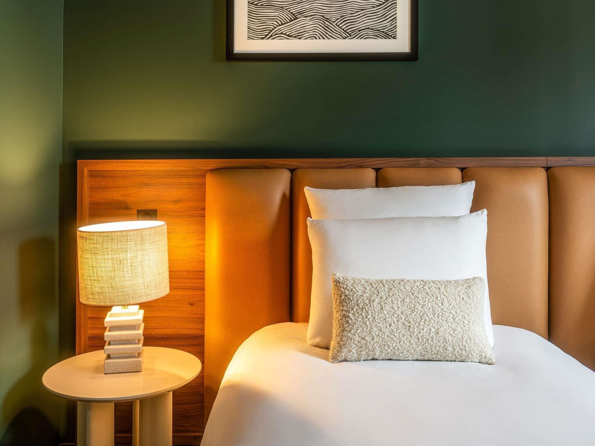 Un lit bien fait, avec une tête de lit, une lampe de chevet et un tableau encadré accroché au mur.