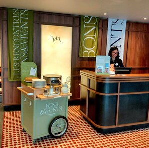 A hotel reception area with a cart labeled 'Bons & Vivants' and a sign above it.