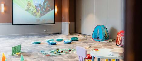 Una sala de conferencias con una pantalla grande, una zona de juegos infantiles y una mesa con sillas.