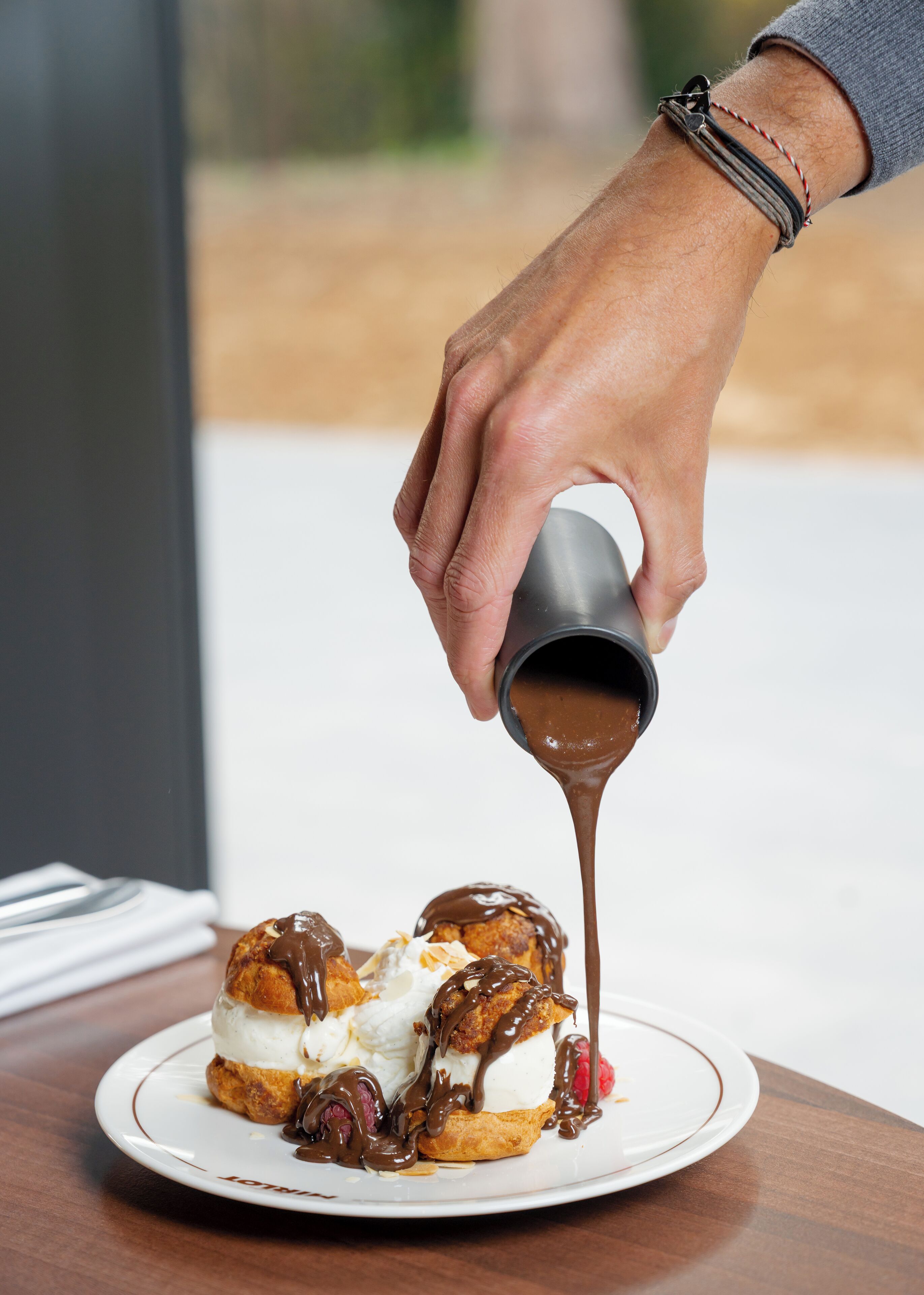 A hand pouring chocolate sauce over dessert on a plate.