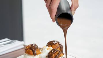 A hand pouring chocolate sauce over dessert on a plate.