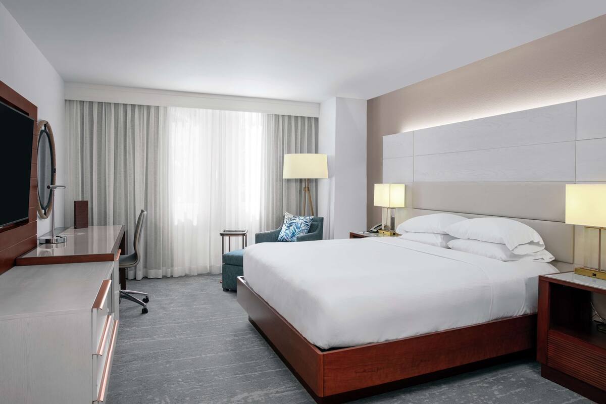 A hotel room with a large bed, a desk, a chair, and a TV.