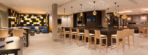 A modern bar area with a long counter, multiple bar stools, and a seating area with a sofa and chairs. - DoubleTree by Hilton Deerfield Beach Boca Raton (Deerfield Beach)