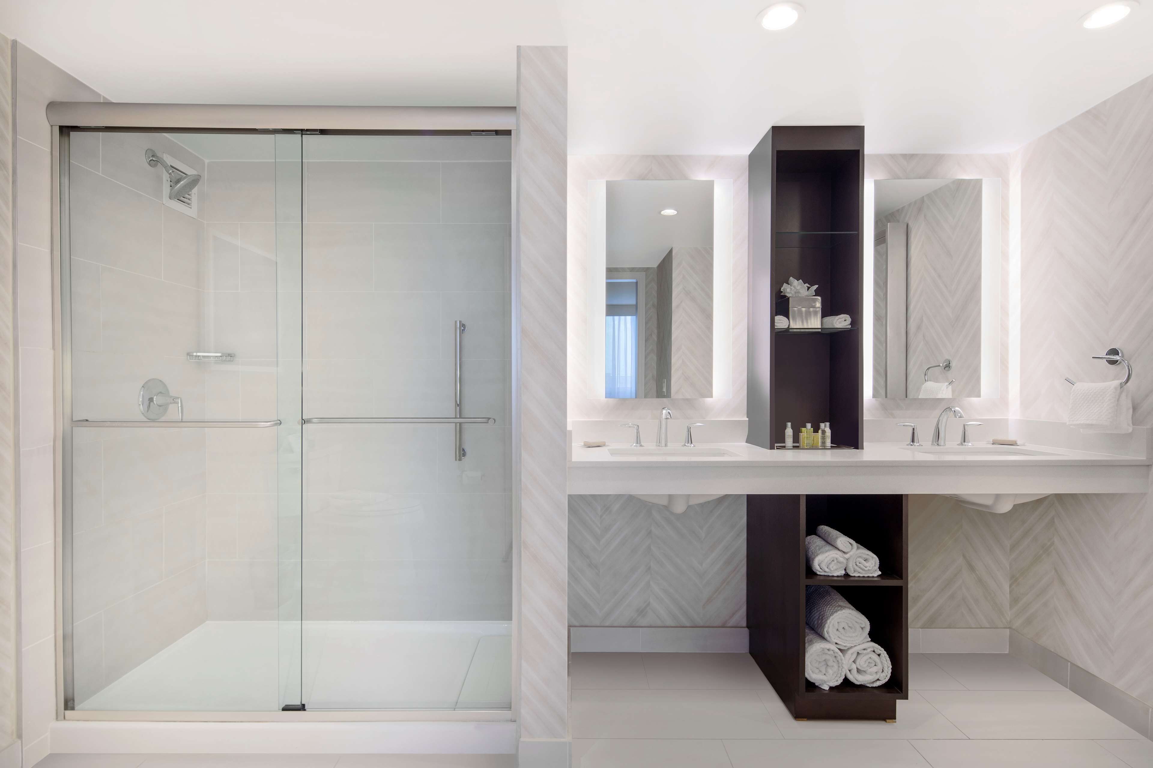 A modern bathroom with a glass-enclosed shower, a vanity with two sinks, and a mirror above the sink.