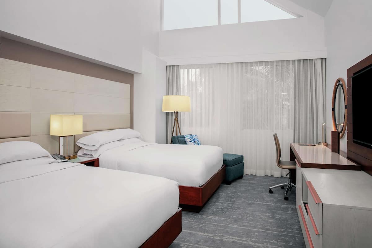 A hotel room with two beds, a desk, a chair, a TV, and a window with curtains.