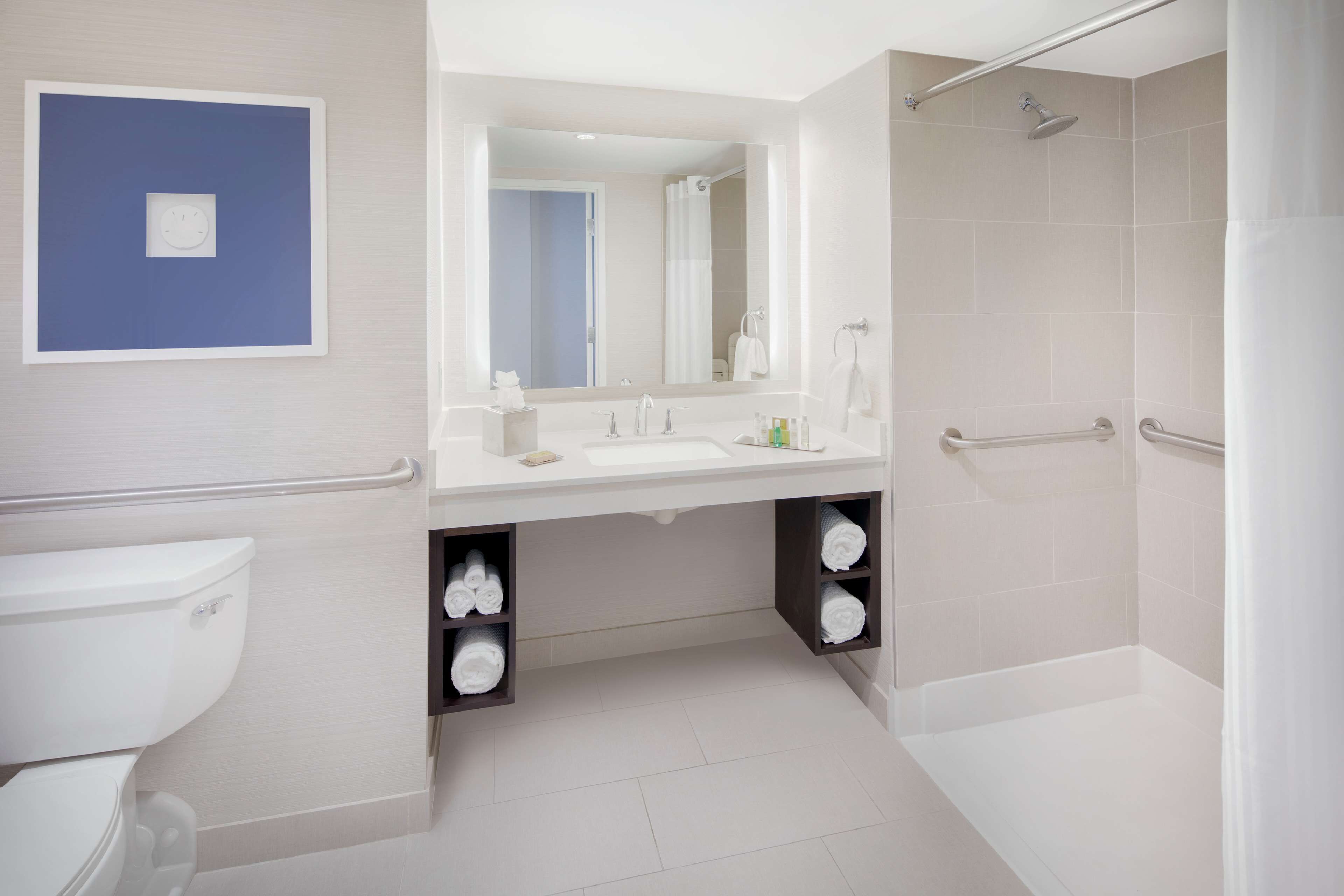 A modern bathroom with a toilet, sink, and shower. There are shelves under the sink for towels.