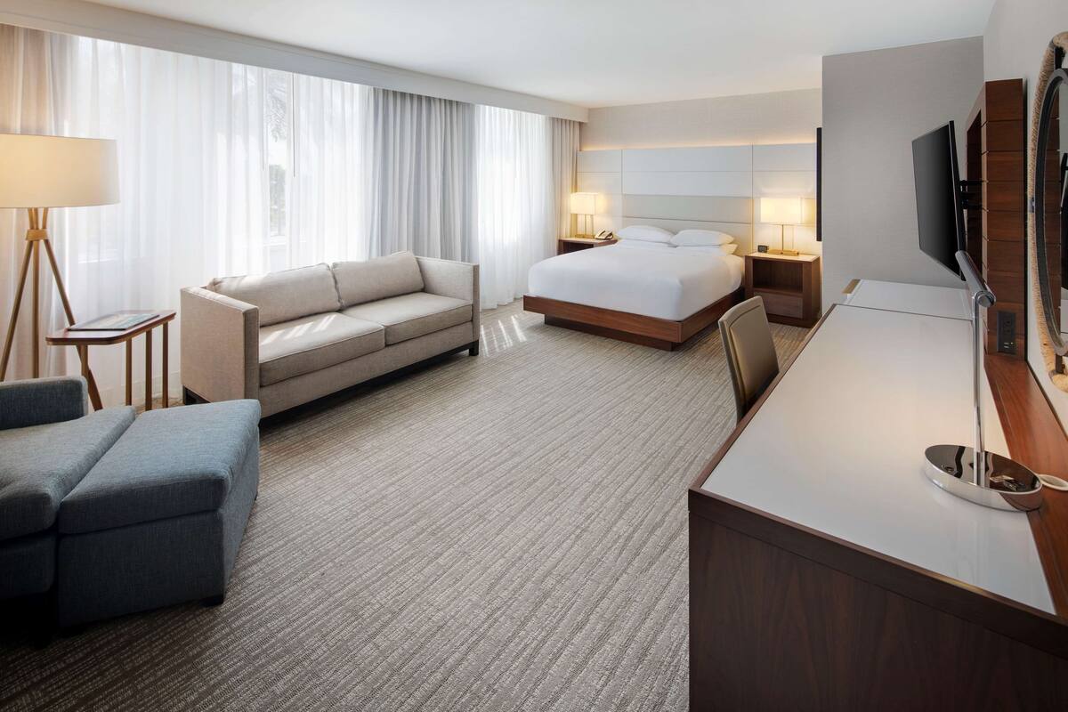 A hotel room with a bed, a sofa, a desk, and a TV.