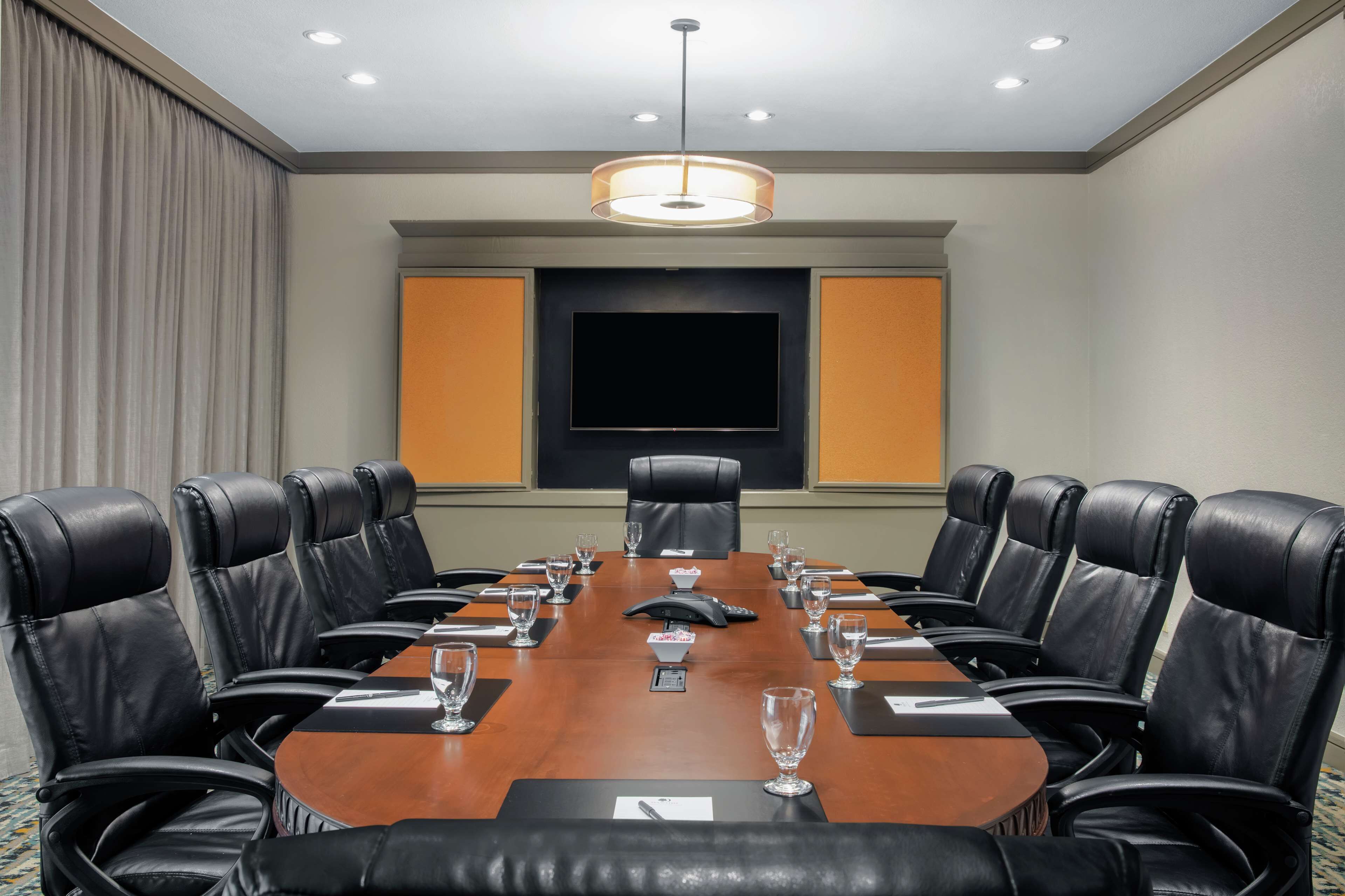 A conference room with a long table, black leather chairs, a large screen, and a ceiling light fixture.