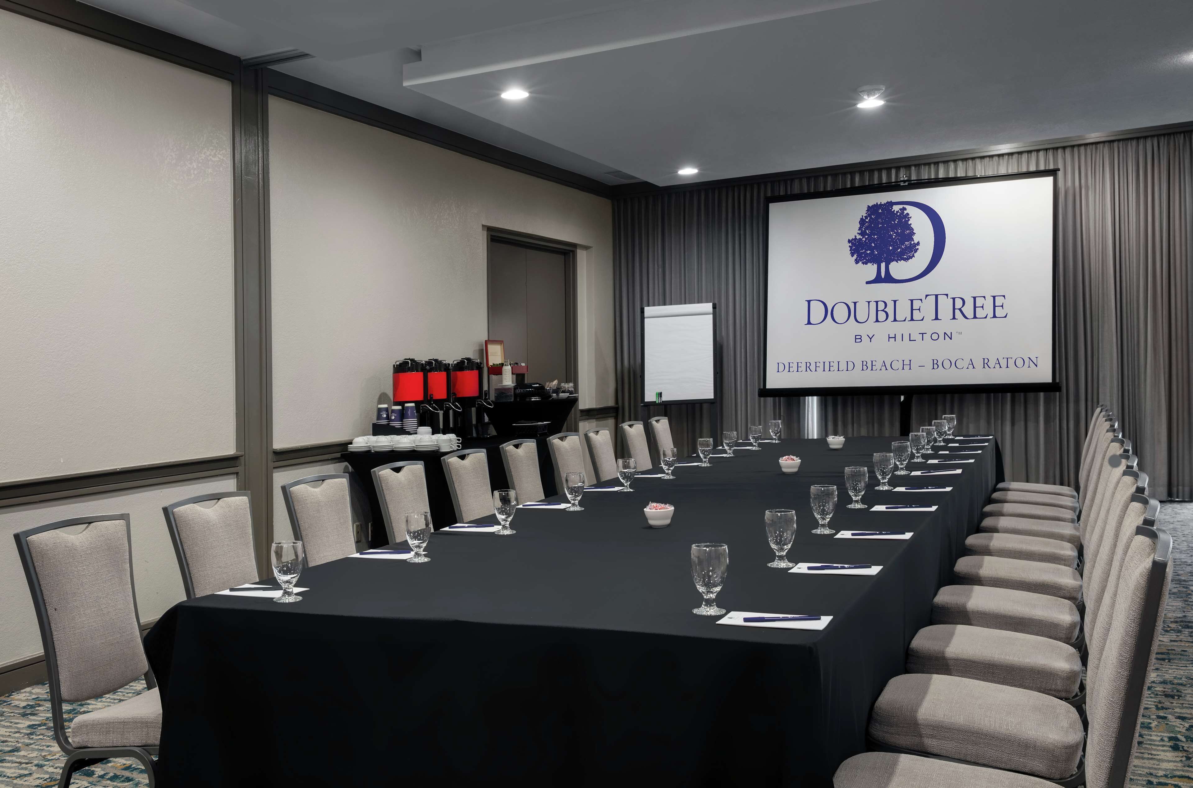 Ein Konferenzraum mit einem langen Tisch, Stühlen und einem Bildschirm, auf dem das DoubleTree-Logo zu sehen ist.
