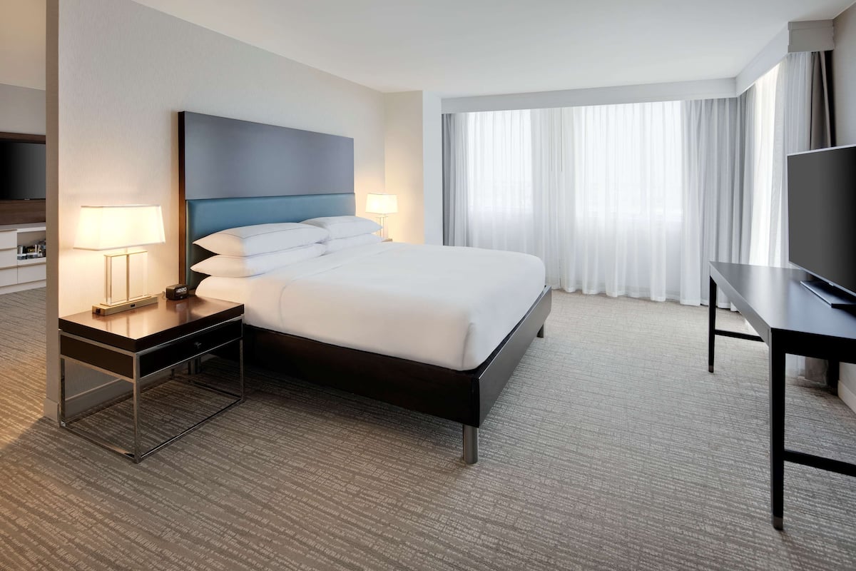 A hotel room with a bed, a desk, a TV, and a window with curtains.