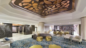A spacious lobby with a modern design, featuring a large seating area with sofas and armchairs, a patterned carpet, and a decorative ceiling. - DoubleTree by Hilton Deerfield Beach Boca Raton (Deerfield Beach)