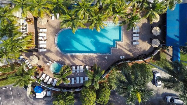 An aerial view of a resort with a central swimming pool, surrounded by palm trees and sun loungers. - DoubleTree by Hilton Deerfield Beach Boca Raton (Deerfield Beach)