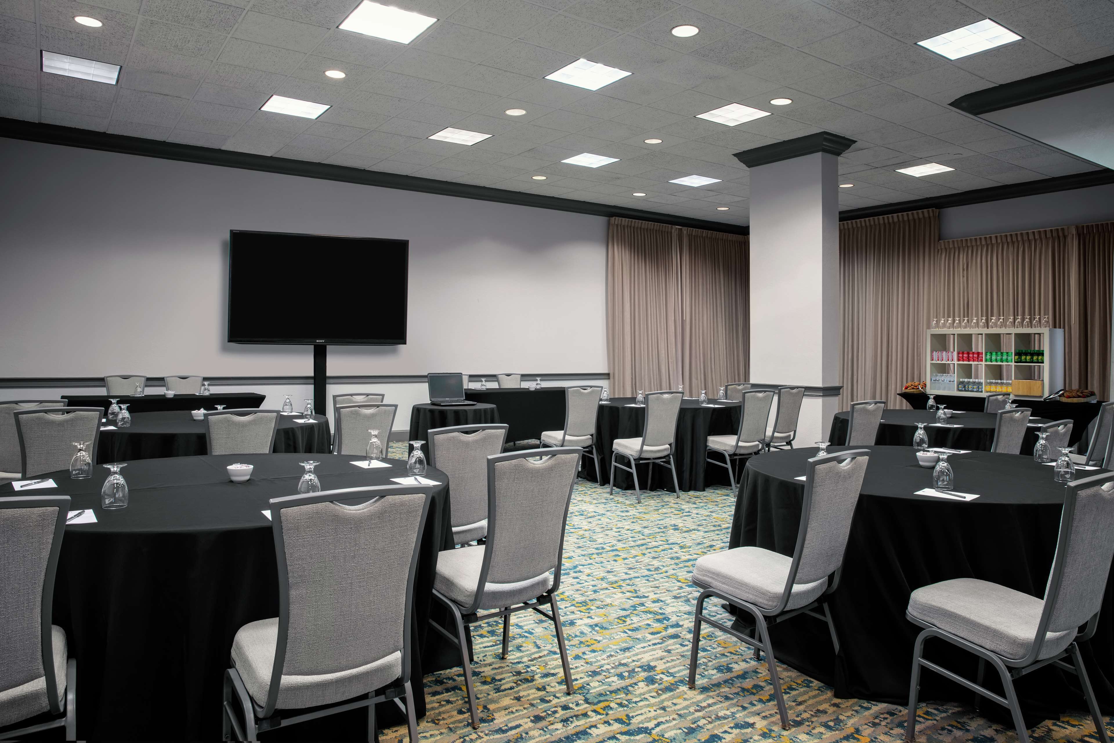 A conference room with round tables, chairs, a flat-screen TV, and a buffet area.