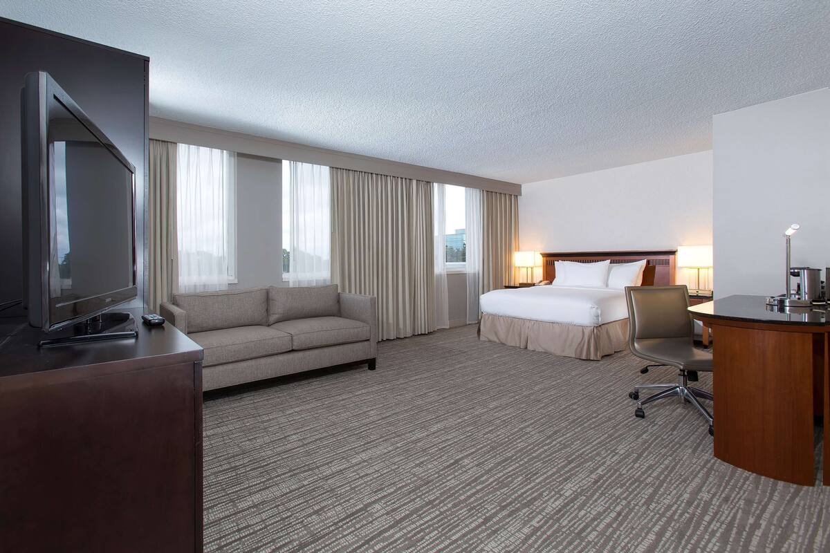 A hotel room with a bed, a sofa, a desk, a TV, and a lamp.