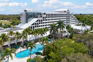 A large hotel with a modern design, featuring a swimming pool surrounded by palm trees and a view of the surrounding landscape. - DoubleTree by Hilton Deerfield Beach Boca Raton (Deerfield Beach)