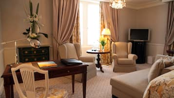 Ein Hotelzimmer mit Schreibtisch, zwei Sesseln, einer Couch, einem Fernseher und einer Chandelier.