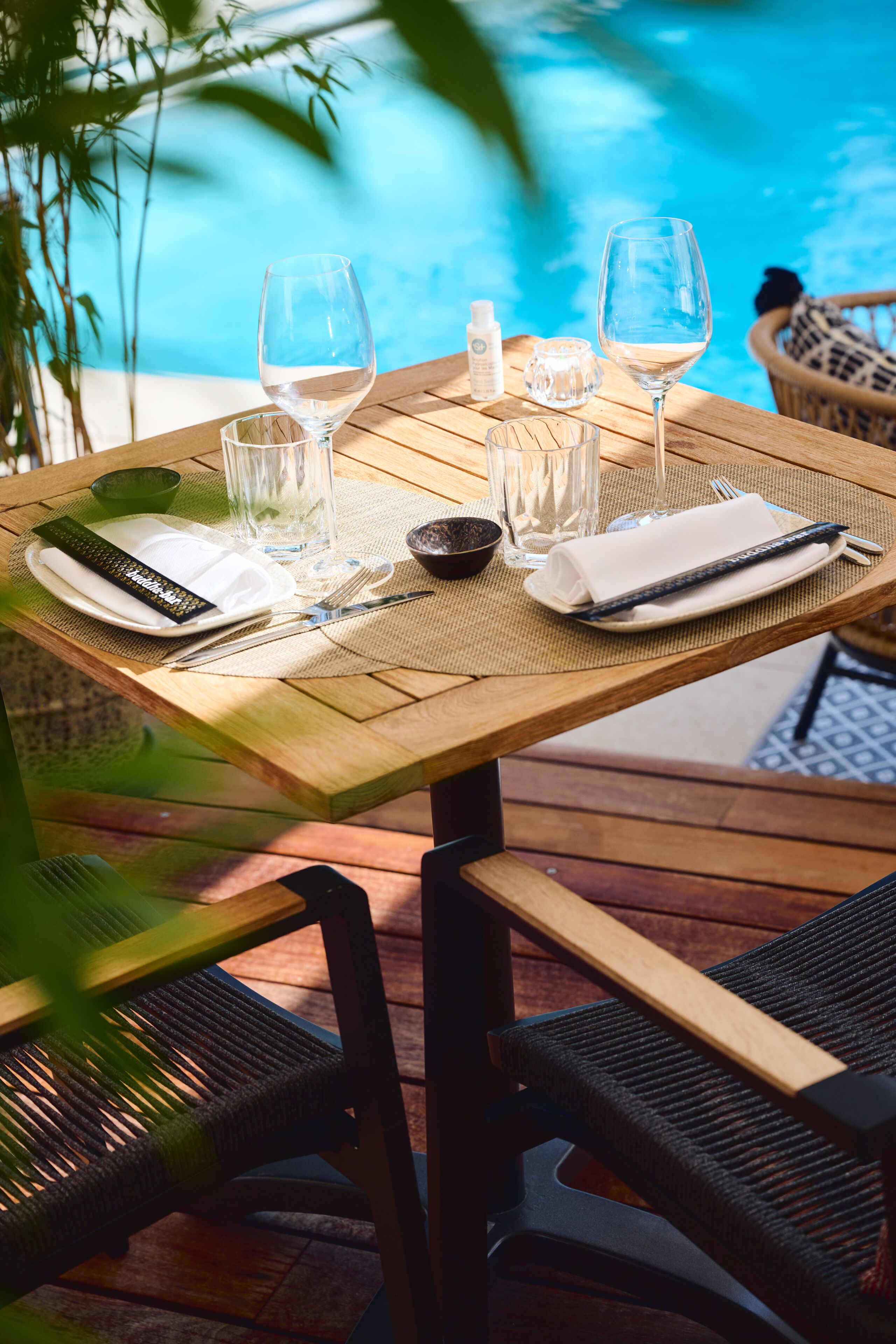 A wooden table set for two with wine glasses, a bottle of water, and a small bowl.